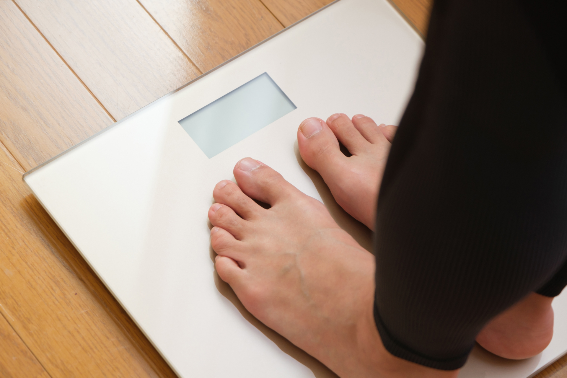 食べていないのに痩せない悩みで体重計を確認する女性